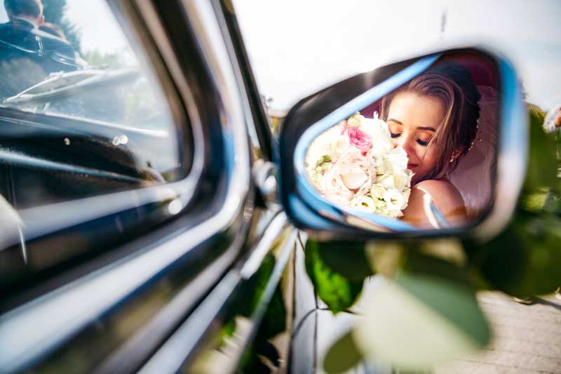 Novia riflessa sullo specchietto del suo coche de alquiler para bodas