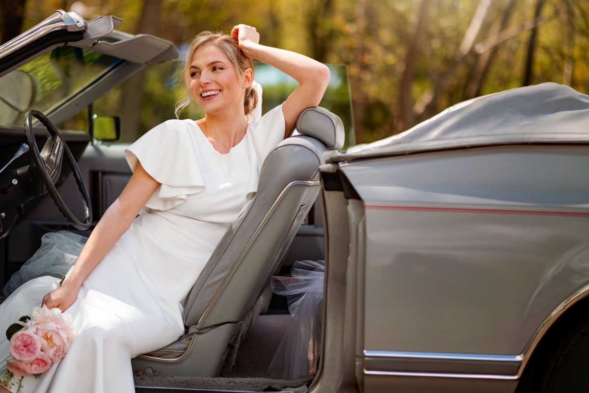 Bride waiting for the driver is sitting on the car she rented for her wedding in Barcelona